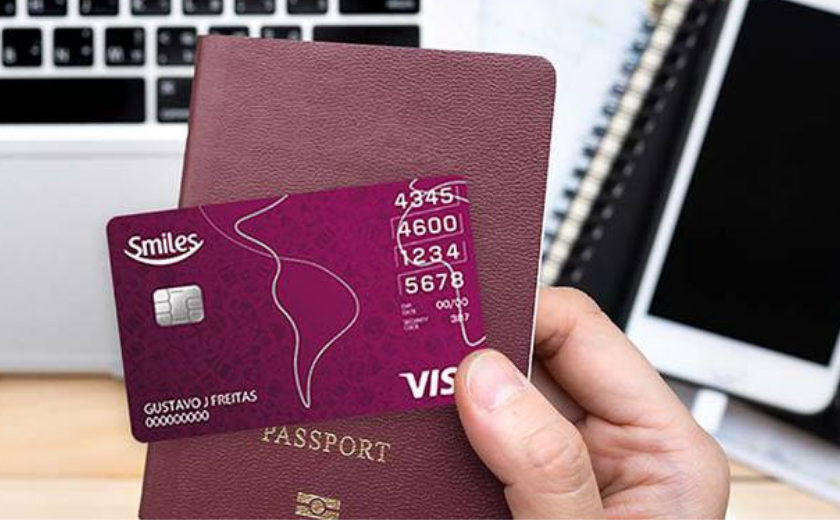 uma mão segurando o cartão bradesco smiles visa internacional e um passaporte