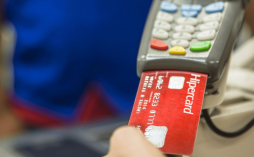 uma mão colocando o cartão de crédito Hipercard Internacional em uma maquininha de cartão